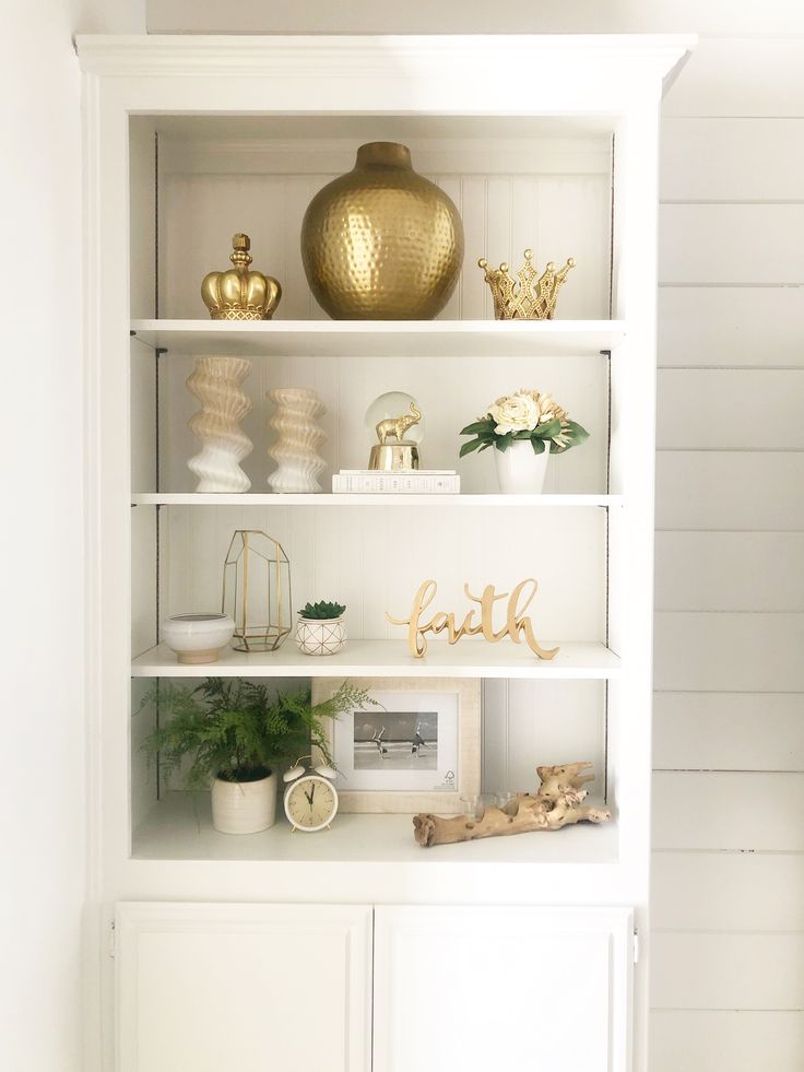 a white bookcase with gold decorations and other items on it's shelves in a living room