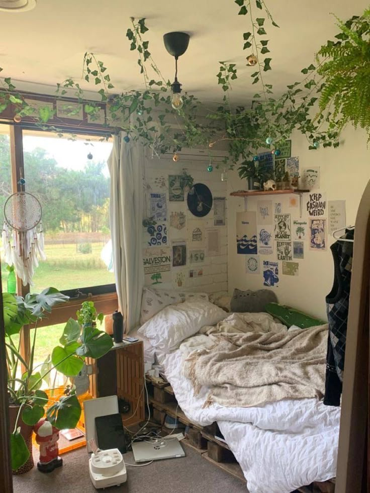 an unmade bed sitting next to a window in a room with lots of plants