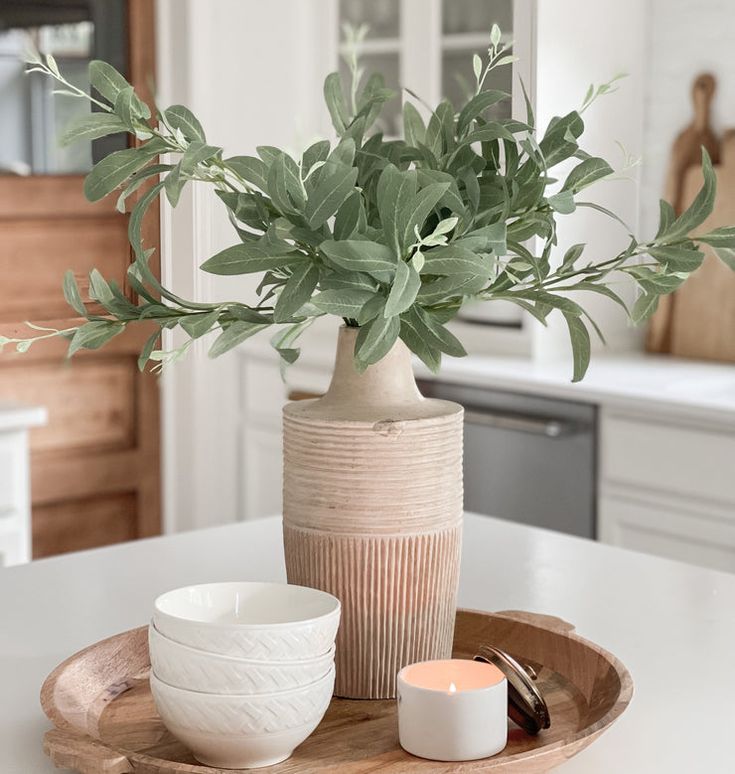 a plant in a ceramic vase on a wooden tray next to two white bowls and a candle