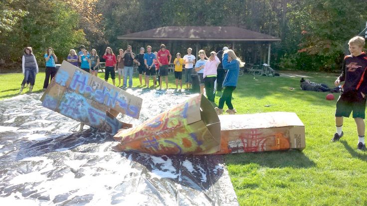 a group of people standing in the grass next to an upside down box with graffiti on it