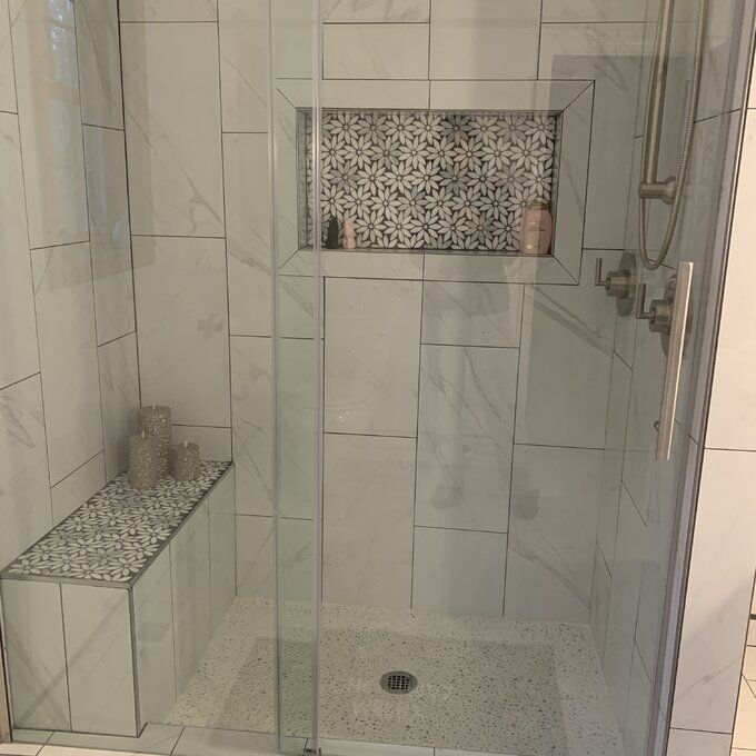 a walk in shower sitting next to a white tiled wall and floor with glass doors