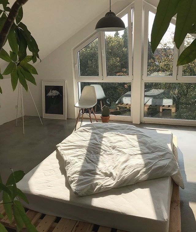 an unmade bed sitting in the middle of a room next to two large windows