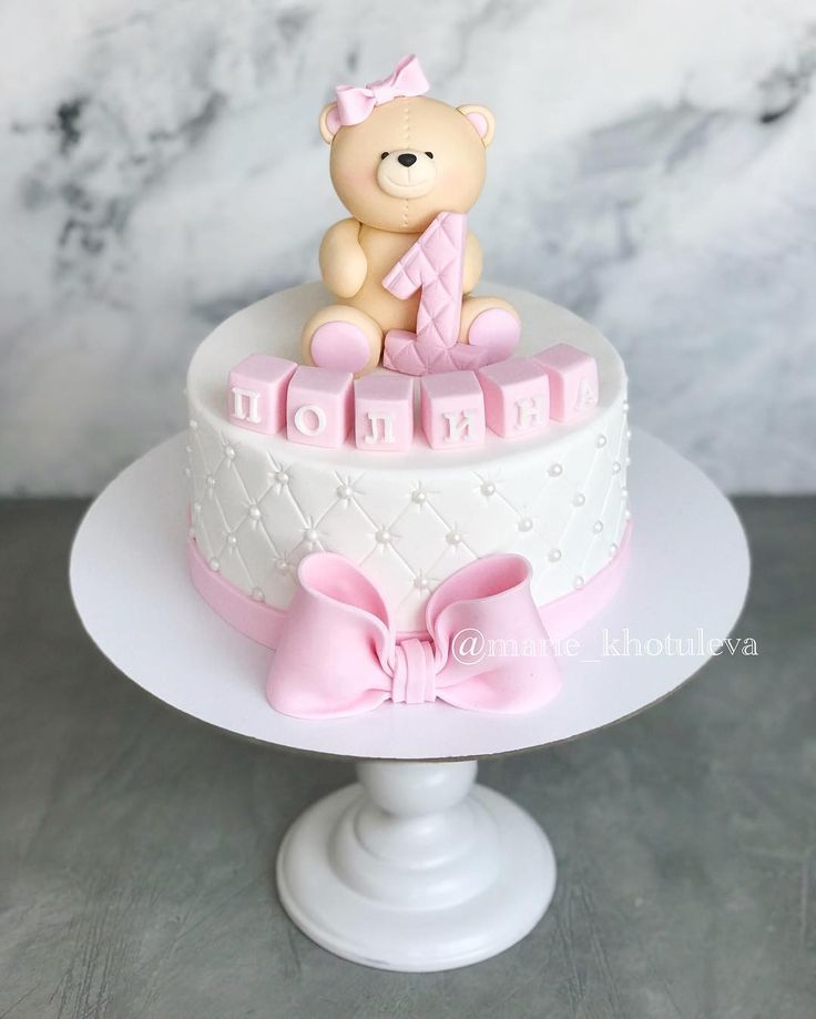 a teddy bear sitting on top of a pink and white cake