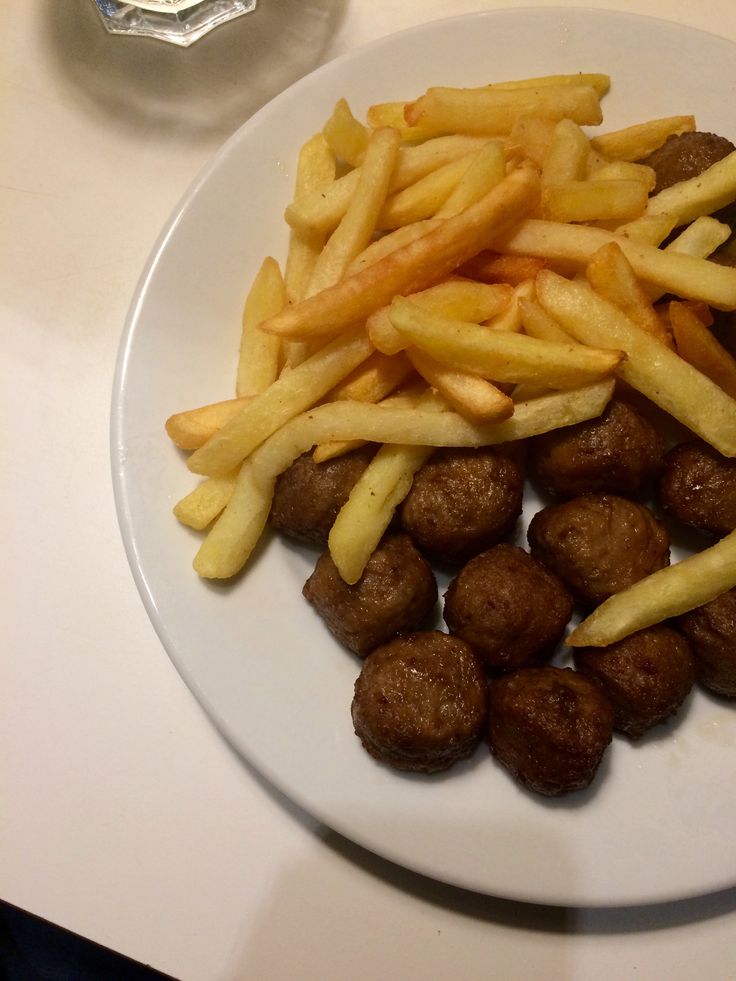 a white plate topped with french fries and meatballs next to a glass of water