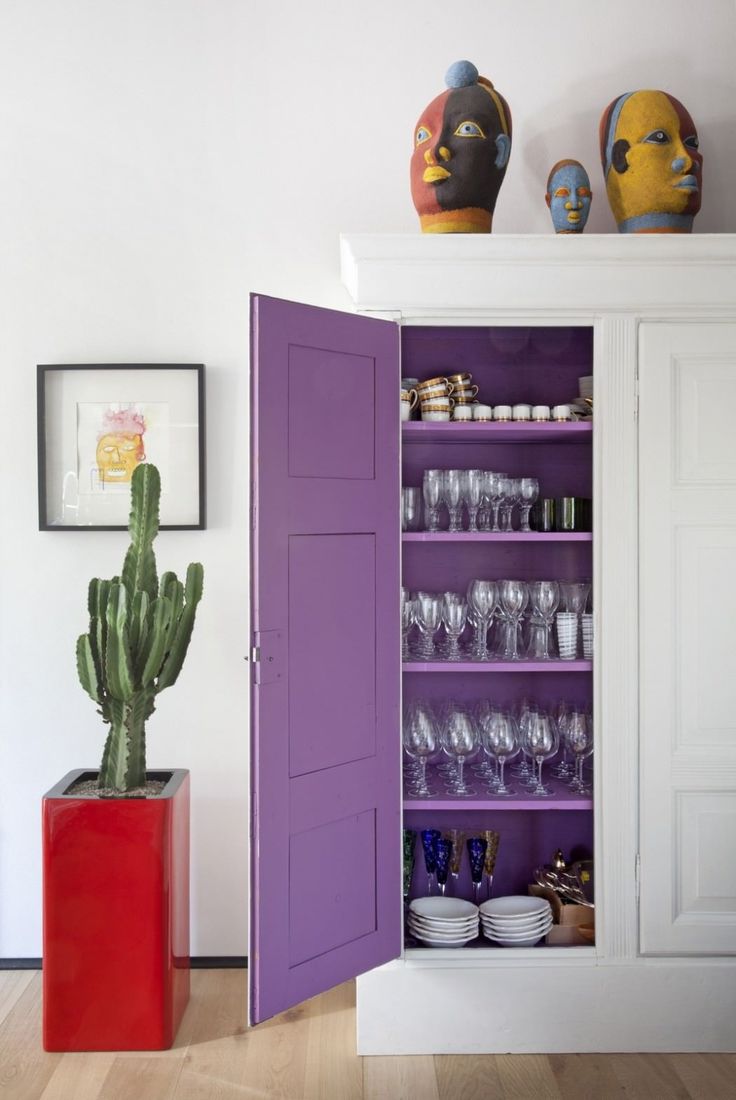 a purple cabinet with wine glasses and a cactus in it next to pictures on the wall