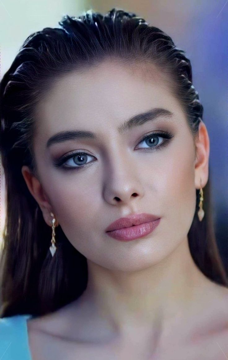 a beautiful woman with blue eyes and long hair wearing gold earrings, looking at the camera