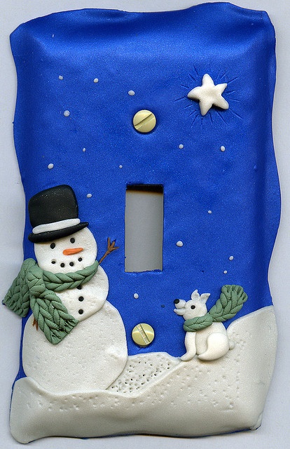 a blue light switch cover with a snowman and dog on it's side