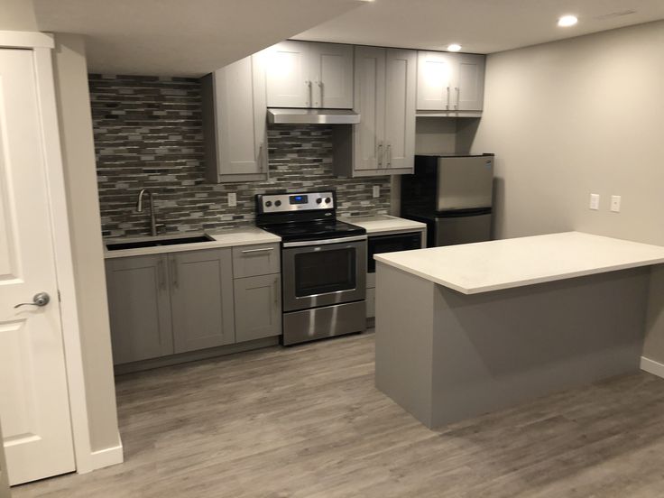 an empty kitchen with stainless steel appliances and white counter tops, along with gray cabinets