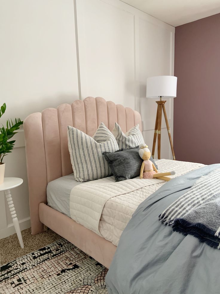 a bedroom with a pink headboard and pillows on the bed next to a lamp