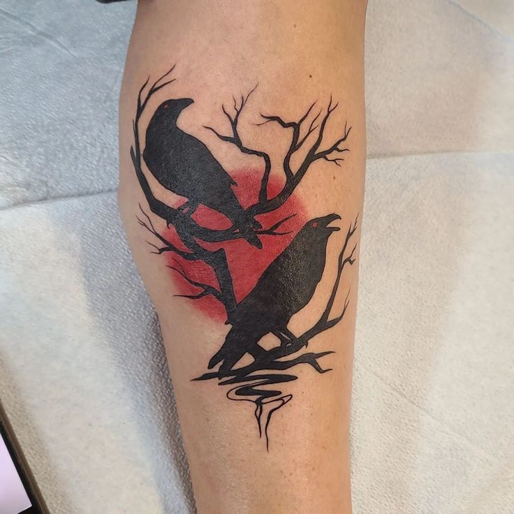 a black bird sitting on top of a tree branch next to a red sun tattoo