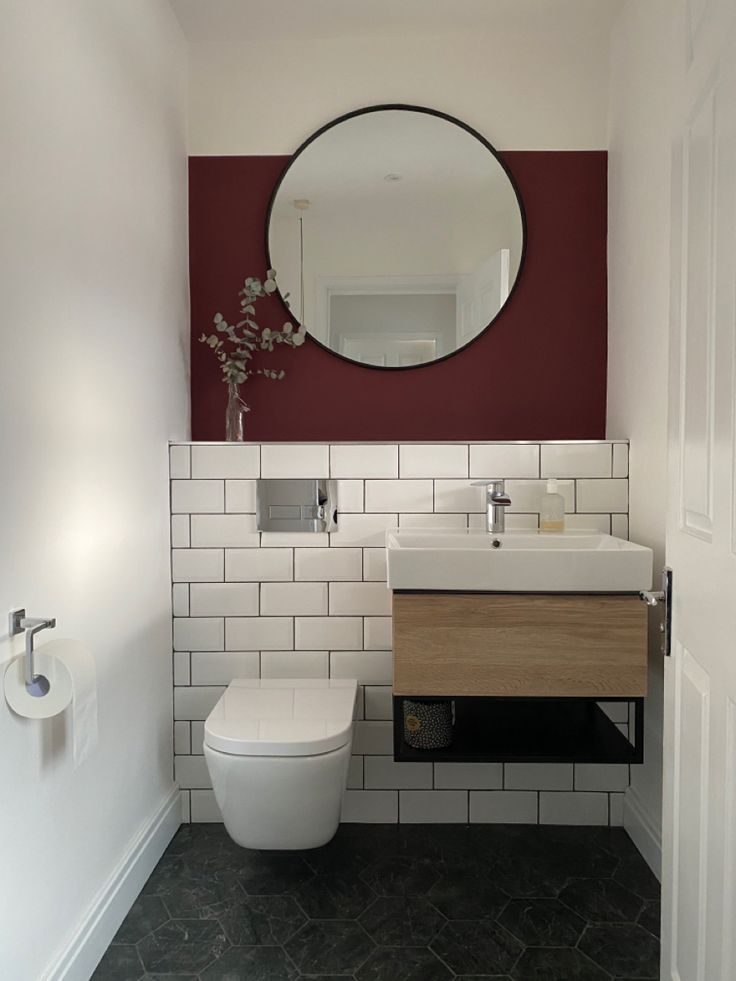 a white toilet sitting next to a bathroom sink under a round mirror on a wall