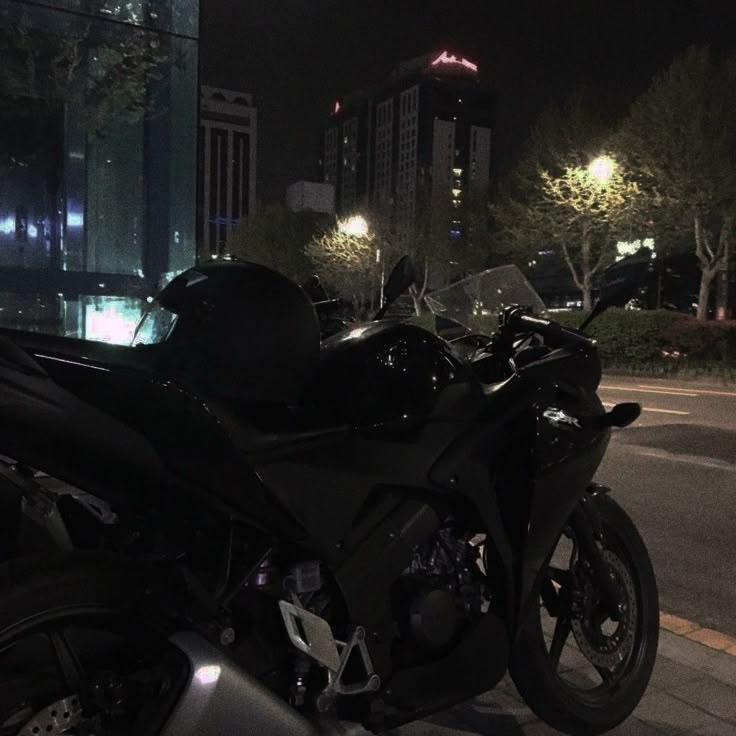 a black motorcycle is parked on the side of the road at night in front of some buildings