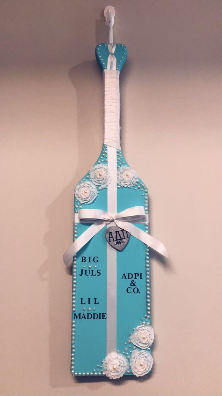 a bottle shaped like a cross hanging on the wall with ribbon and tag attached to it