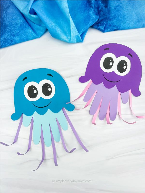 two paper cutouts with eyes and arms on a white surface, one is purple and the other is blue