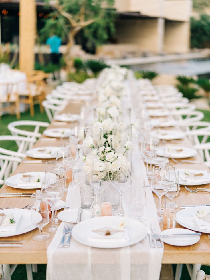 a long table is set with white flowers and place settings for an outdoor wedding reception