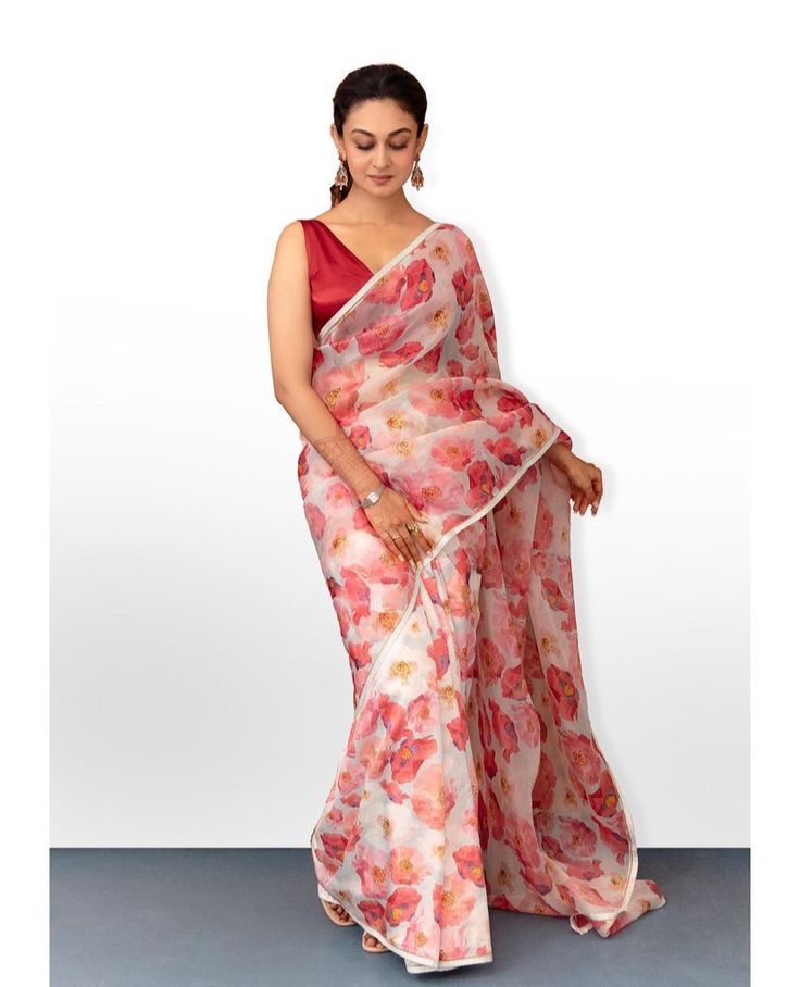 a woman in a red and white sari with flowers on the border, standing against a