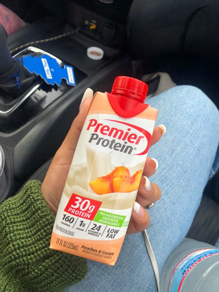 a person holding a carton of protein drink in their hand while sitting in a car