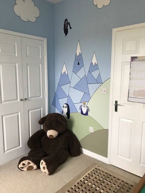 a large teddy bear sitting in the corner of a room with mountains painted on the wall