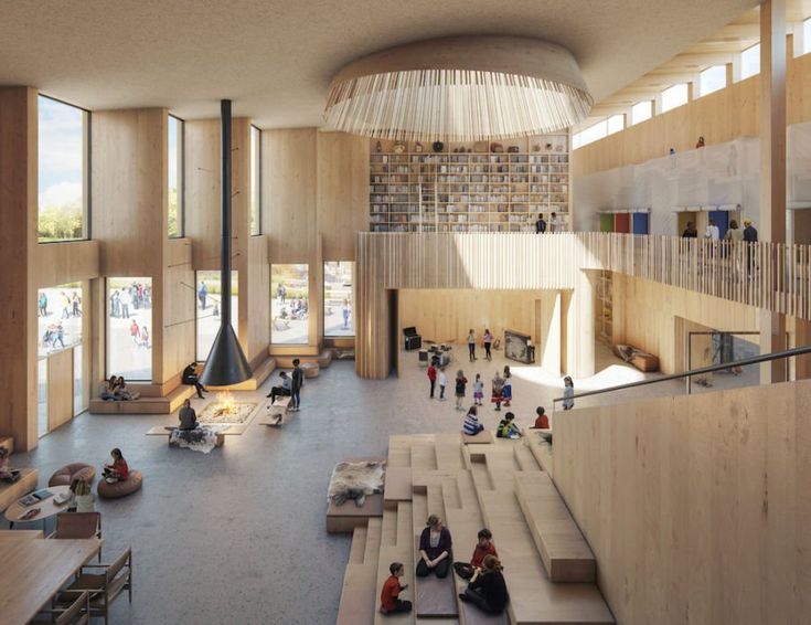 people are sitting and standing in a large room with stairs, bookshelves, and windows