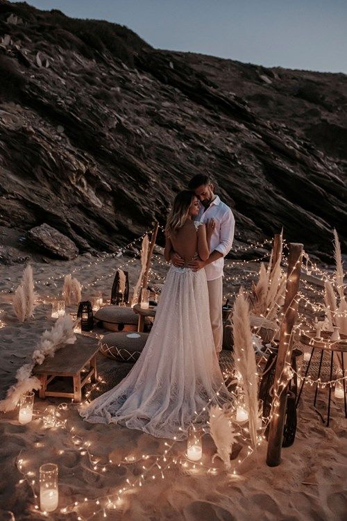 a man and woman standing next to each other on top of a sandy beach covered in lights