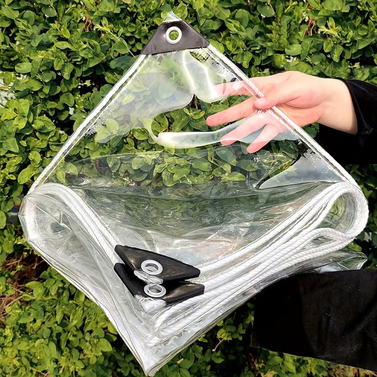 a person holding a clear bag with scissors and other items in it on top of some bushes