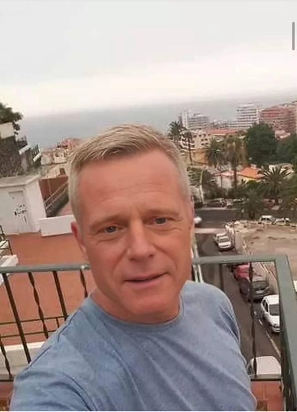 a man standing on top of a balcony next to a street filled with parked cars