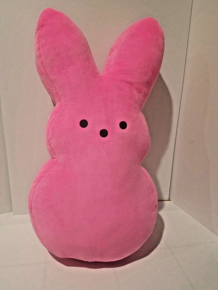 a pink bunny pillow sitting on top of a white counter next to a wall with black eyes