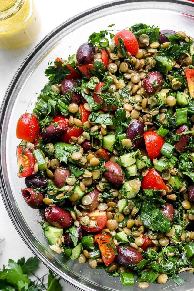 a salad in a glass bowl on top of a white table with tomatoes, cucumbers and other vegetables