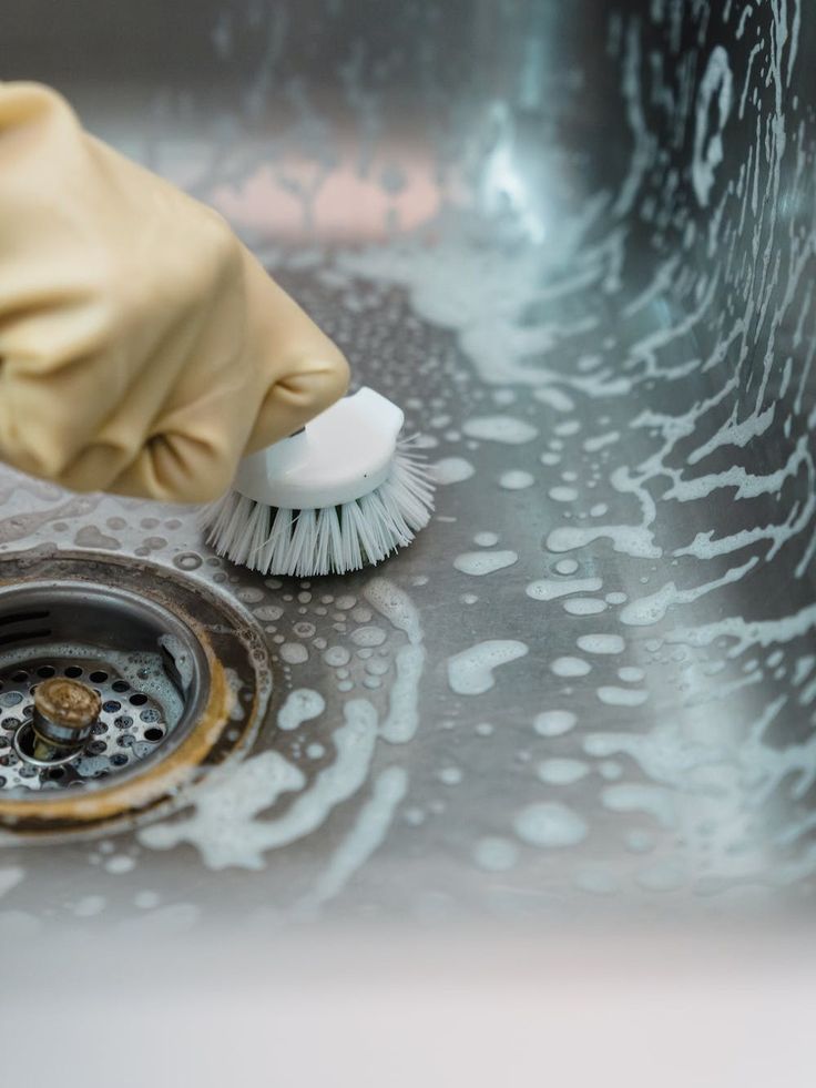 a person in yellow gloves and rubber gloves cleaning a sink with a white scrubber