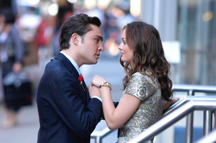 a man and woman standing next to each other in front of a metal railing looking at each other