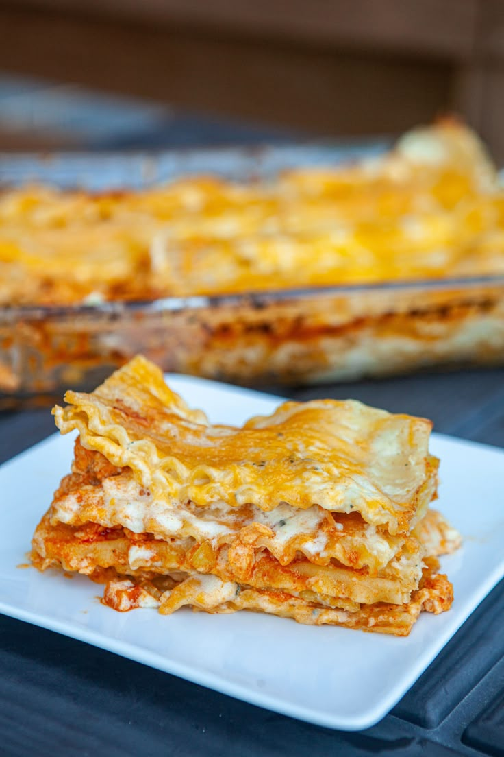 a white plate topped with lasagna next to a casserole dish