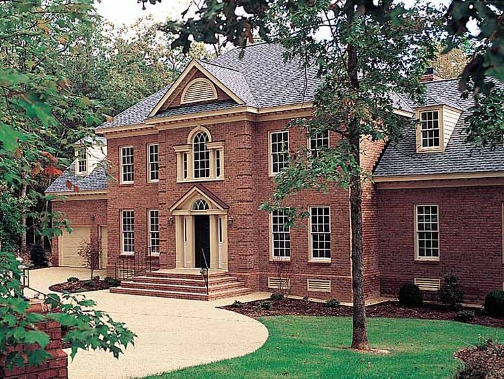 a large brick house with lots of windows on it's sides and trees in the front yard