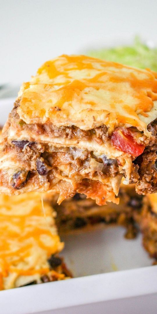 a piece of lasagna being lifted from a casserole dish with lettuce on the side