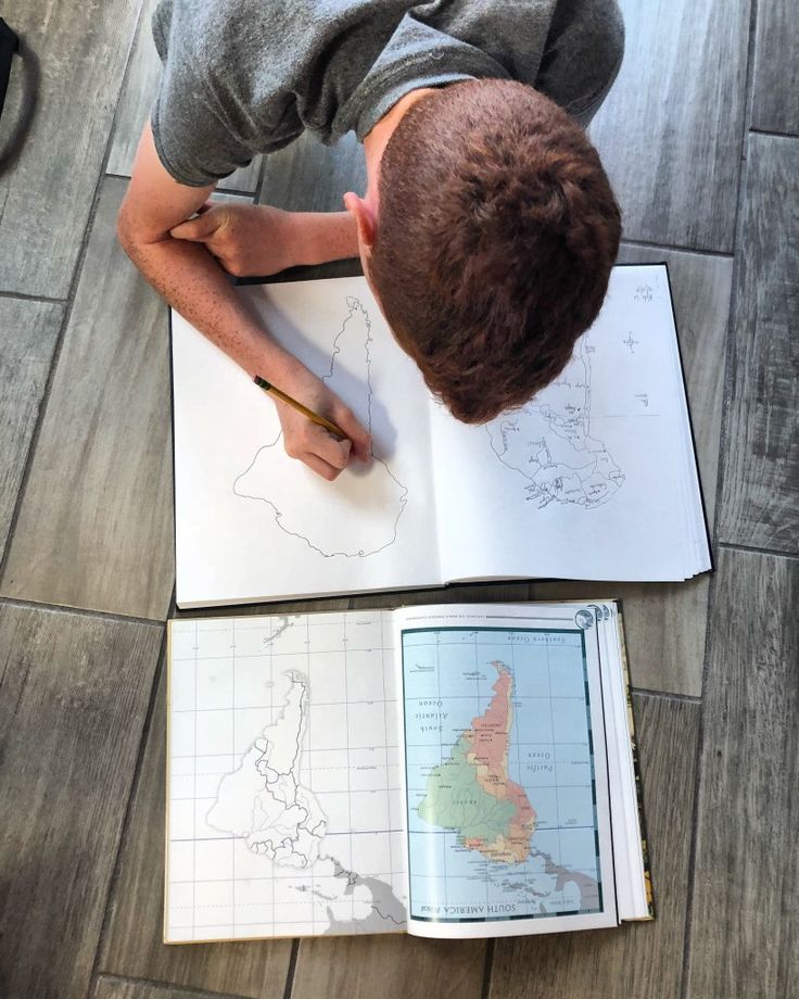 a young man is writing on a map while sitting at a table with an open book