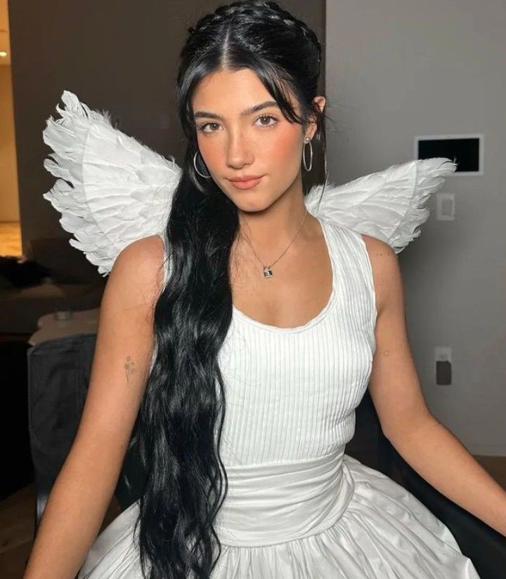 a woman with long black hair wearing a white dress and angel wings on her head