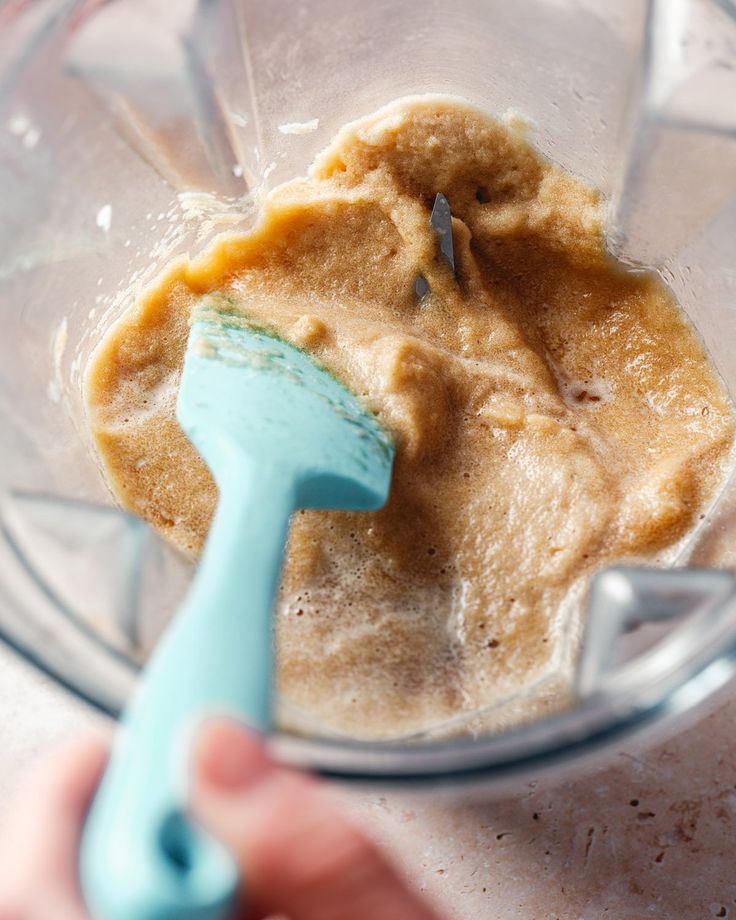 someone is mixing something in a blender with a blue plastic spatula to stir it