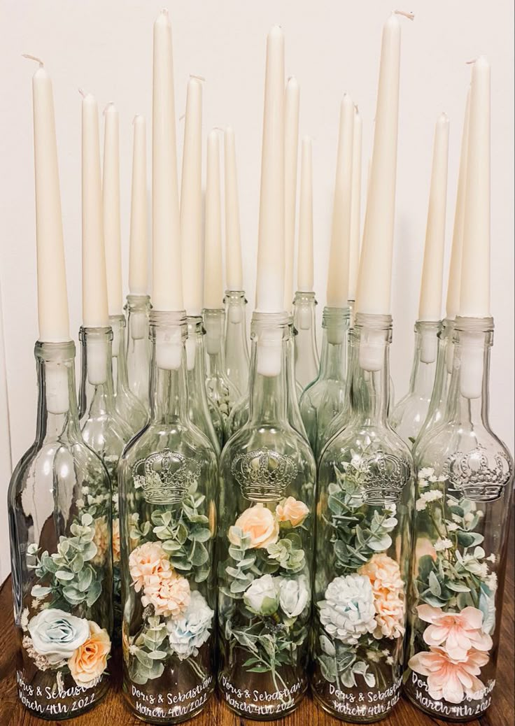 there are many bottles with flowers in them and candles on the table next to each other