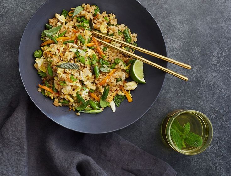 a black plate topped with rice and veggies next to two chopsticks