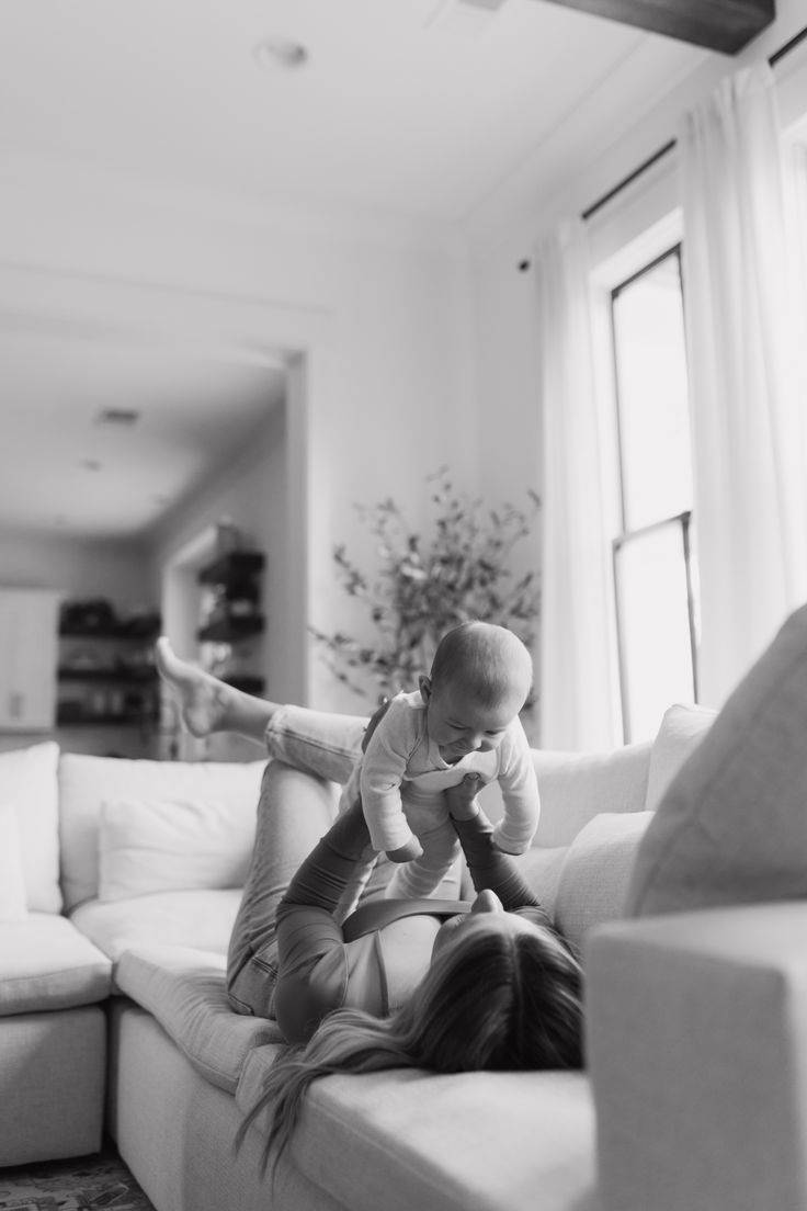 a woman holding a baby while sitting on top of a couch in a living room