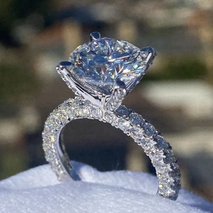 a close up view of a diamond engagement ring on top of snow covered ground with trees in the background