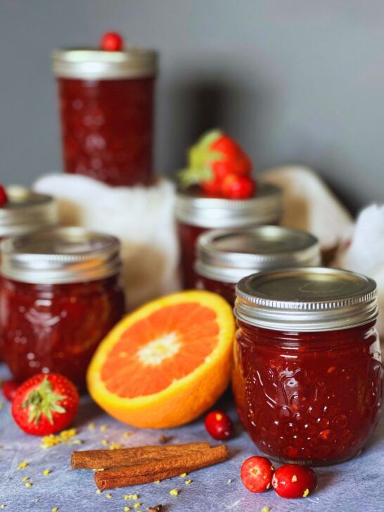 several jars filled with jam sitting on top of a table next to oranges and strawberries