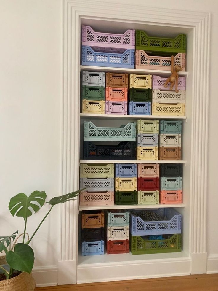 a white book shelf filled with lots of colorful boxes next to a potted plant