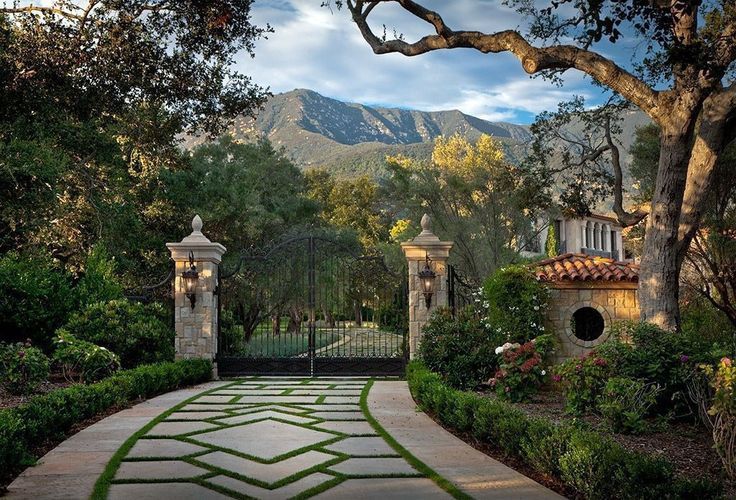 an entrance to a home surrounded by lush green trees and shrubbery with mountains in the background