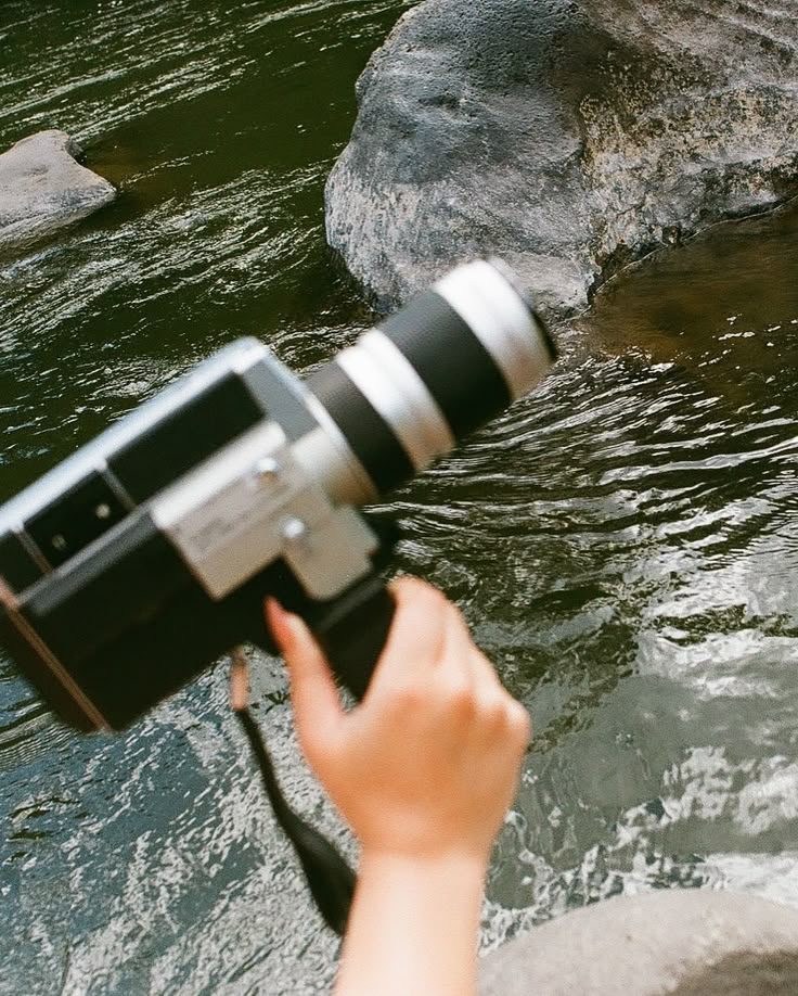 a person holding a camera up to take a photo in the water with rocks behind them