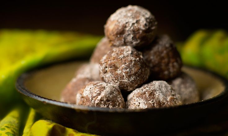 a bowl filled with chocolate covered doughnuts on top of a table next to bananas