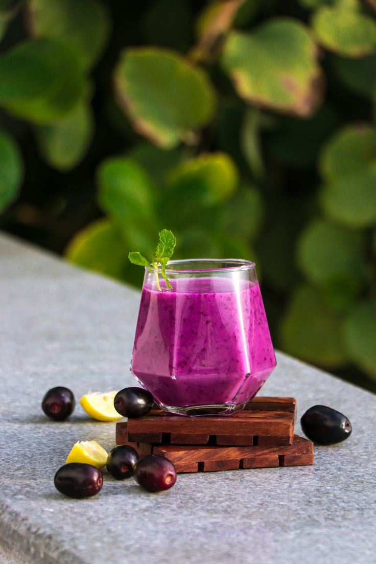 a glass filled with purple liquid sitting on top of a wooden block