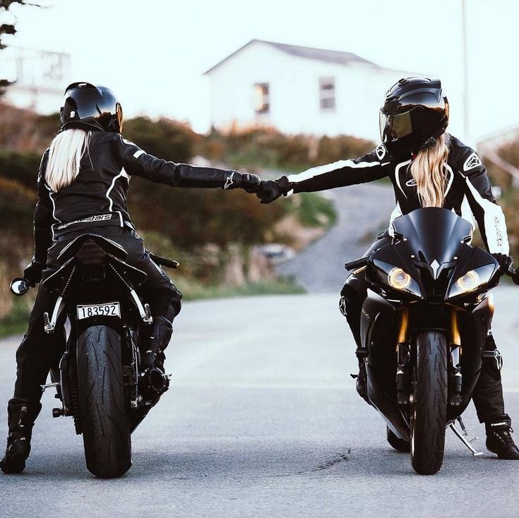 two motorcyclists are riding down the road holding each other's hands