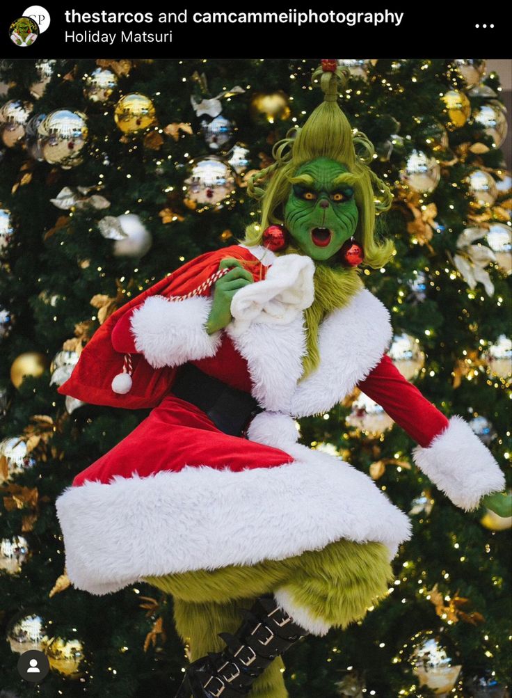 a person dressed as the grinch standing in front of a christmas tree