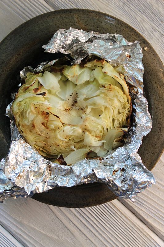 an artichoke wrapped in aluminum foil sitting on top of a black plate next to a wooden table