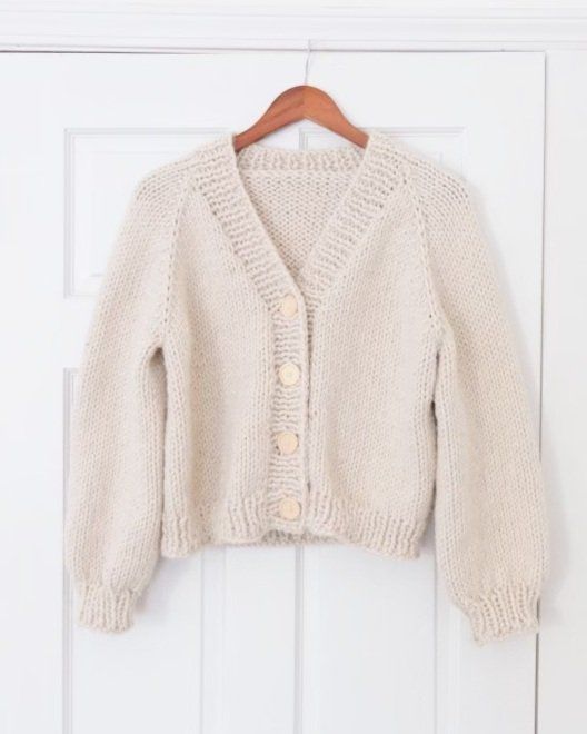 a white sweater hanging on a door with a wooden hanger in front of it